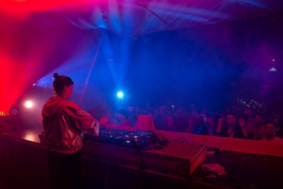 Eine DJ spielt an einem Mischpult vor einer begeisterten Menge. Bunte Lichter und Nebel schaffen eine lebhafte Stimmung. | © Monique_Fessl