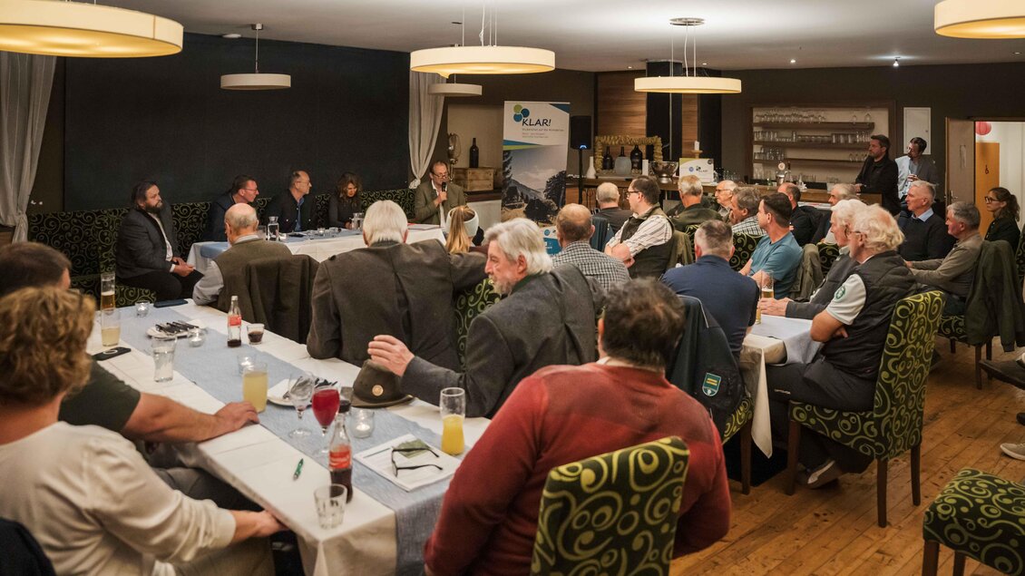 Eine Menschenmenge sitzt an einem großen Tisch in einem Restaurant. Im Vordergrund findet eine Diskussion statt, während die Teilnehmer aufmerksam zuhören. | © NUP Eisenwurzen