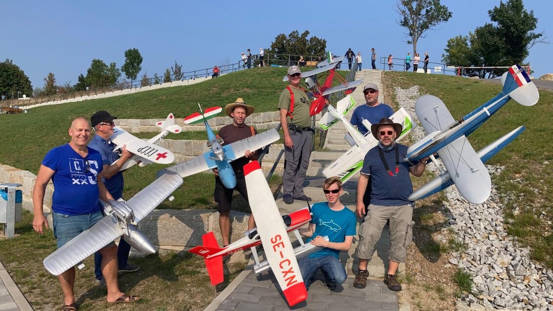 Eine Gruppe von Menschen steht auf einem Weg und hält verschiedene ferngesteuerte Flugzeuge. Im Hintergrund sind weitere Personen und eine grüne Landschaft zu sehen. | © Modell Wasserflugverein Lausitz e. V.