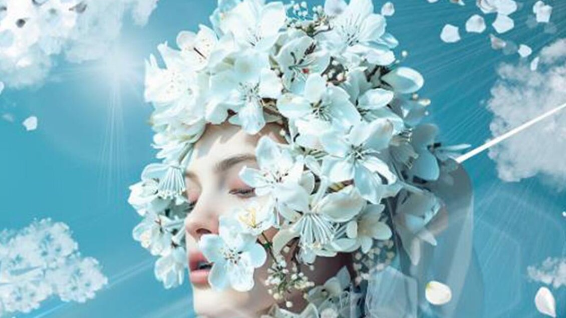 Ein Porträt einer Person mit einem Kopfschmuck aus weißen Blumen. Der Hintergrund ist in sanften Blautönen gehalten, was eine traumhafte Stimmung erzeugt. | ©  Segafredo Leoben