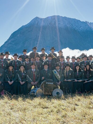 A brass band is playing on an outdoor stage. The musicians are wearing traditional clothing in red and black. | © Trachtenkapelle Tauplitz