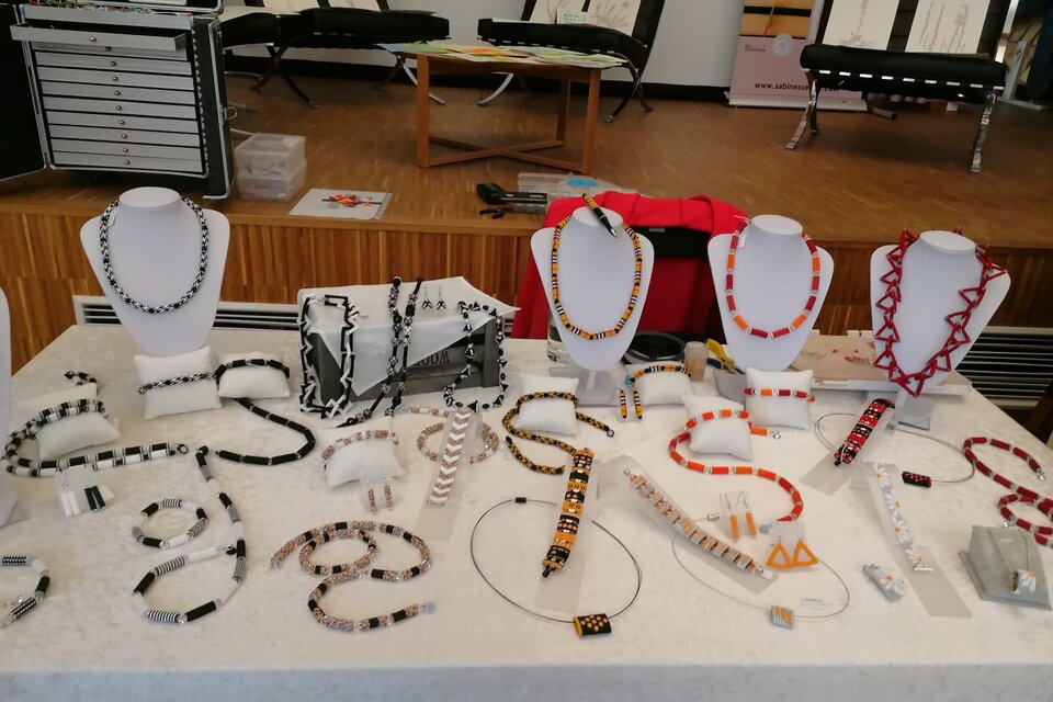 Ein Tisch mit einer Auswahl an Schmuckstücken, darunter Halsketten und Armbänder in verschiedenen Farben und Designs. Die Schmuckstücke sind auf Ständern ausgestellt und bestehen aus unterschiedlichen Materialien. | © Susanne Braun