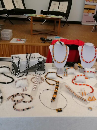 A table with a selection of jewelry pieces, including necklaces and bracelets in various colors and designs. The jewelry pieces are displayed on stands and made of different materials. | © Susanne Braun