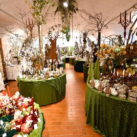 A beautiful shop adorned with various decorations and plants. The tables are covered with green cloths and offer a variety of festive items. | © Tourismusverband Thermen- & Vulkanland/Christian Thomaser