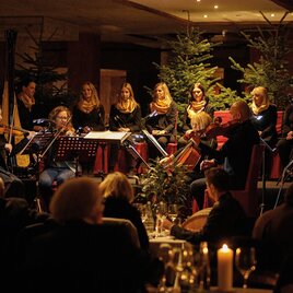 A musical ensemble plays for guests in a festively decorated room. In the background, Christmas trees and candlelight can be seen. | ©  Karl Schrotter Photograph