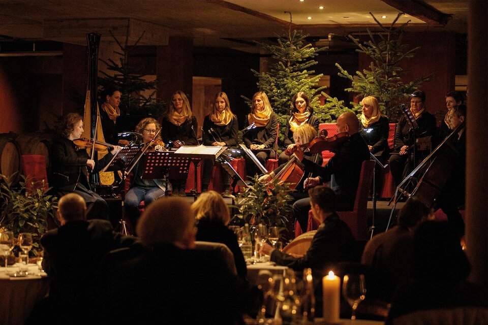 Ein musikalisches Ensemble spielt für Gäste in einem festlich dekorierten Raum. Im Hintergrund sind Weihnachtsbäume und Kerzenlicht zu sehen. | ©  Karl Schrotter Photograph