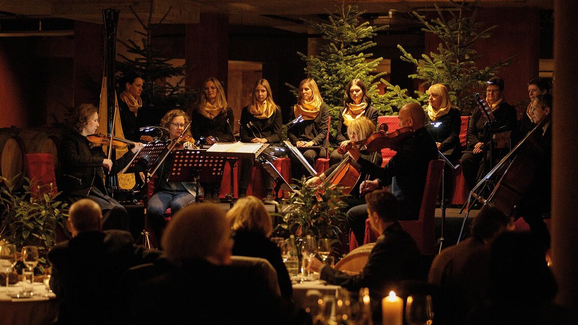 Ein musikalisches Ensemble spielt für Gäste in einem festlich dekorierten Raum. Im Hintergrund sind Weihnachtsbäume und Kerzenlicht zu sehen. | ©  Karl Schrotter Photograph