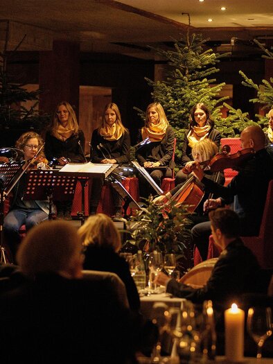 A musical ensemble plays for guests in a festively decorated room. In the background, Christmas trees and candlelight can be seen. | ©  Karl Schrotter Photograph
