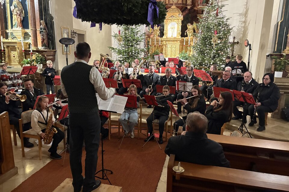 Weihnachtliche Klänge in festlicher Kirchenatmosphäre. Ein Blasorchester mit Musikerinnen und Musikern verschiedener Generationen musiziert unter der Leitung eines Dirigenten vor dem prachtvoll geschmückten Altar der Pfarrkirche Unterlamm. Beleuchtete Christbäume, ein großer Adventkranz und die stimmungsvolle Kulisse sorgen für eine besinnliche Atmosphäre und musikalische Vorfreude auf Weihnachten.

 | © MV Unterlamm