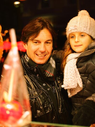 A smiling man and a girl are standing in front of a sales booth. They are looking at various candies in a festive atmosphere. | © Graz Tourismus - Max Wegscheidler