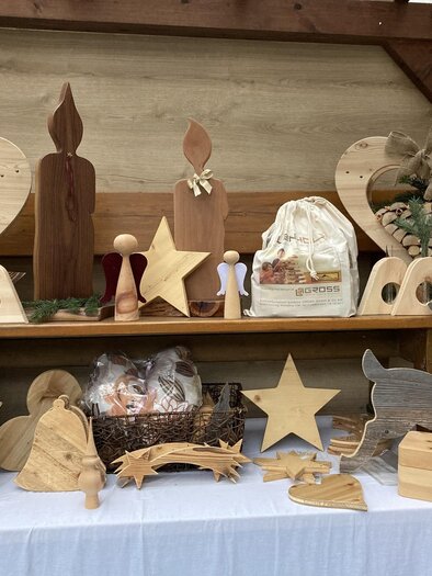 Christmas crafts made of wood with lovingly crafted angels, stars, hearts, candles, and reindeer on a festively decorated Advent stand. | © Samstagmarkt