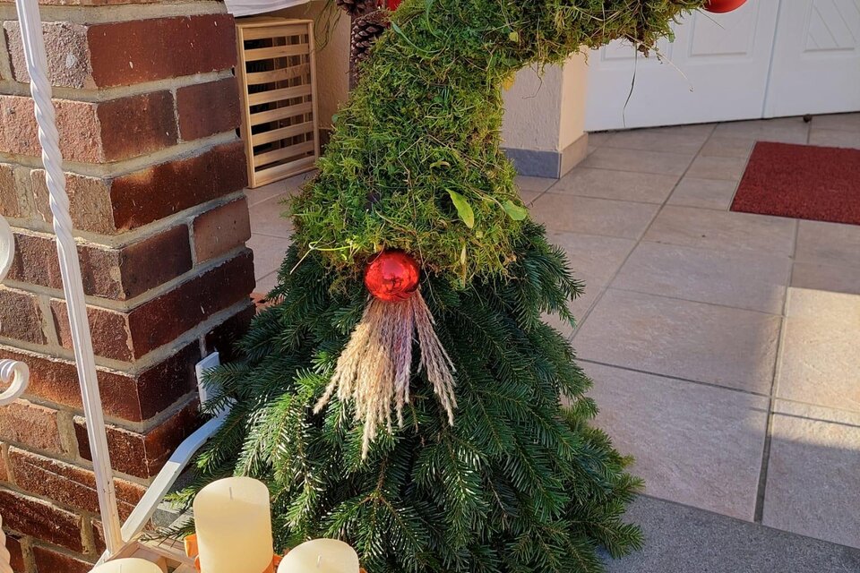 Ein festlich geschmückter Weihnachtsbaum in Form eines Hutes, verziert mit roten Kugeln. Im Vordergrund stehen einige Kerzen in einem rustikalen Arrangement. | © Kalcher Marianne