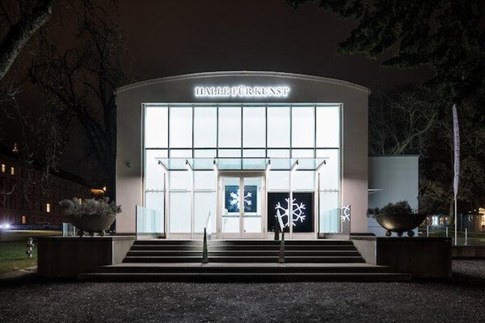 Nächtliche Außenansicht der Halle für Kunst mit beleuchteter Glasfassade, Eingangstreppe und Schneeflockendekoration. | © kunst-dolumentation.com