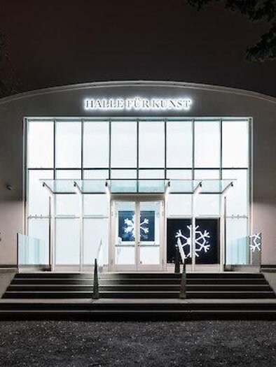 Night view of the Hall for Art with illuminated glass facade, entrance staircase, and snowflake decoration. | © kunst-dolumentation.com