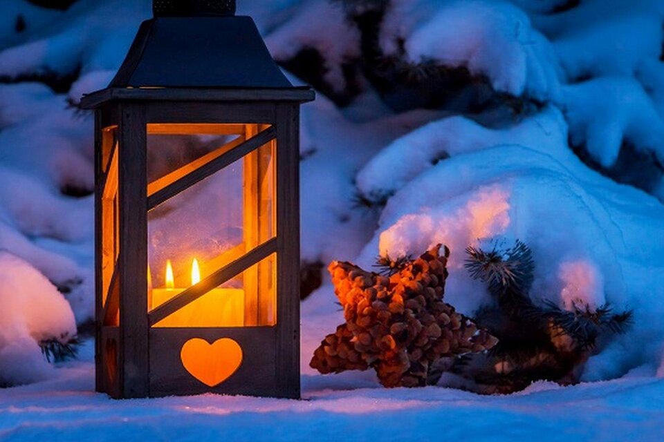 Eine schöne Laterne mit warmem Licht steht im Schnee. Neben der Laterne liegt ein dekorativer Stern aus Tannenzapfen. | © Fotolia