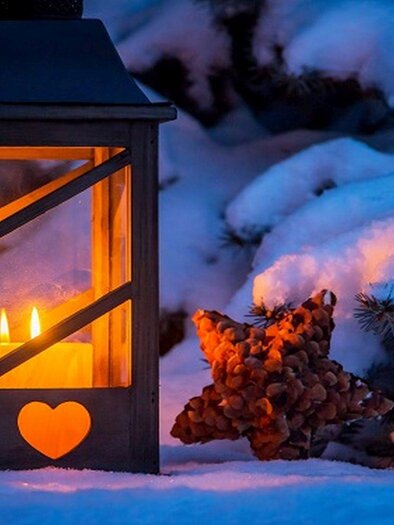 Eine schöne Laterne mit warmem Licht steht im Schnee. Neben der Laterne liegt ein dekorativer Stern aus Tannenzapfen. | © Fotolia