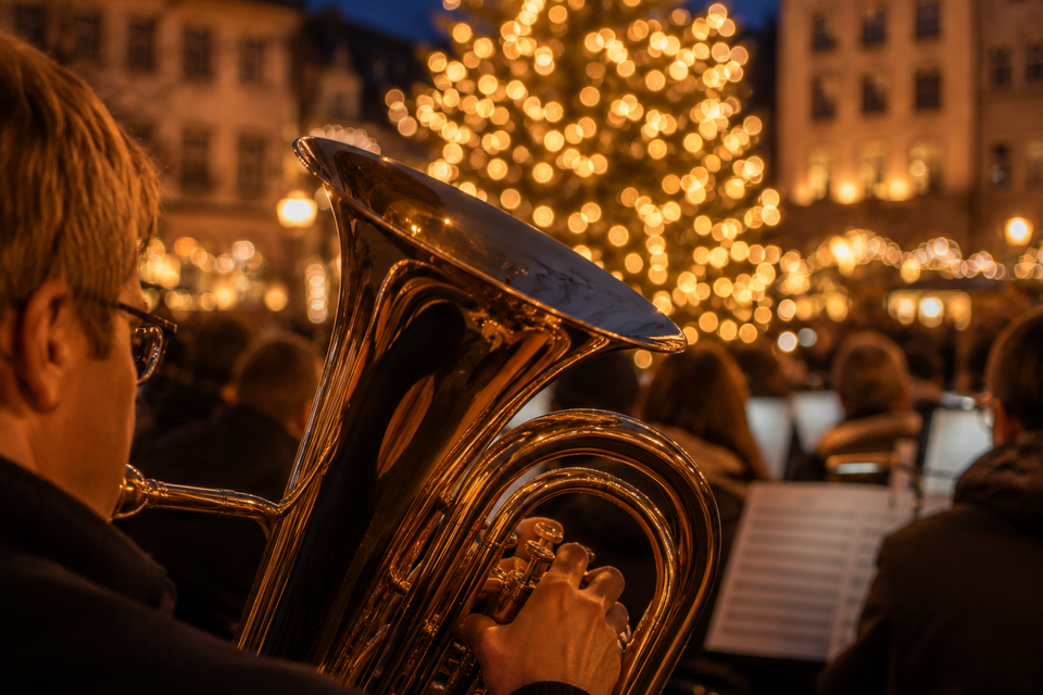 Blasmusiker mit Tuba vor beleuchtetem Weihnachtsbaum bei einem Adventskonzert. | © ChatGPT-Christine Rotschädl