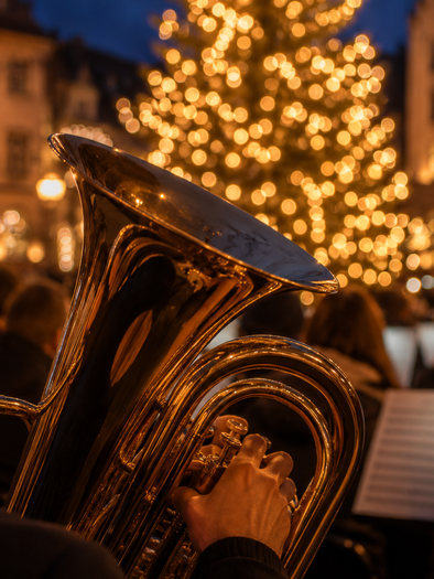 Blasmusiker mit Tuba vor beleuchtetem Weihnachtsbaum bei einem Adventskonzert. | © ChatGPT-Christine Rotschädl