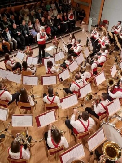 Ein großes Orchester spielt auf einer Bühne. Im Hintergrund sitzt ein Publikum und hört aufmerksam zu. | © Greith Haus