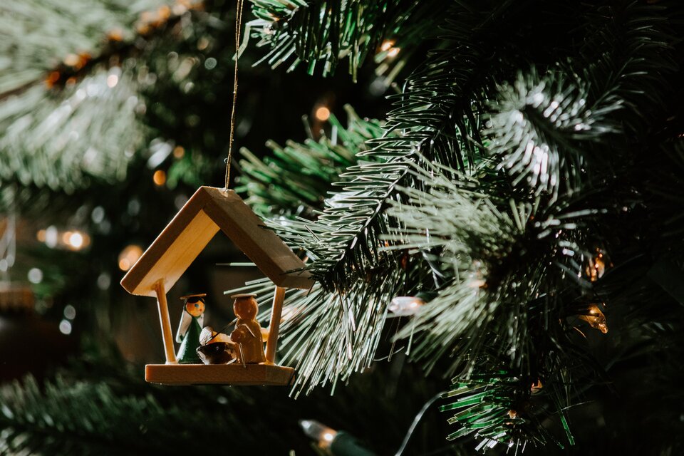 Ein Holzornament in Form eines Hauses hängt an einem Weihnachtsbaum. Darin stehen zwei Figuren, umgeben von grünen Ästen und Lichtern. | © TV Murau