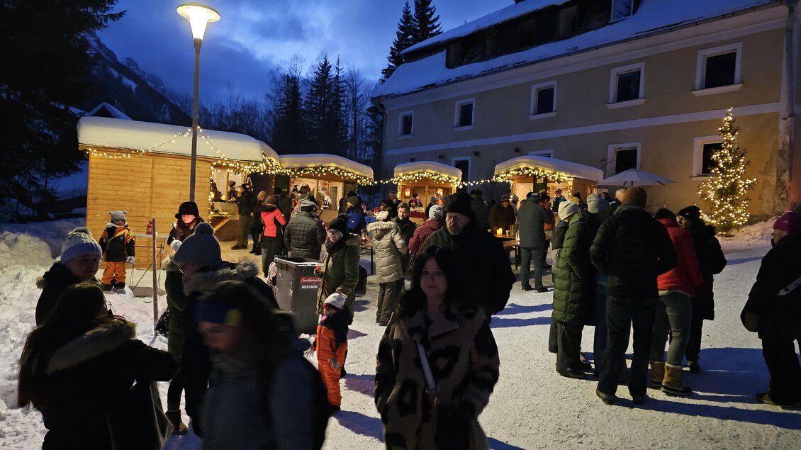 Ein winterlicher Weihnachtsmarkt mit beleuchteten Ständen und zahlreichen Besuchern. Die Umgebung ist schneebedeckt und die Stimmung ist festlich. | © Herbert Bieber