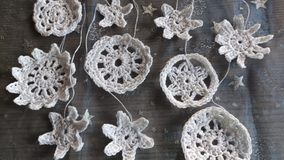 Eine dekorative Anordnung von weißen Häkelmotiven in verschiedenen Formen. Die Motive sind kunstvoll auf einem glitzernden Hintergrund drapiert. | © Gabriele Marchner Trieb