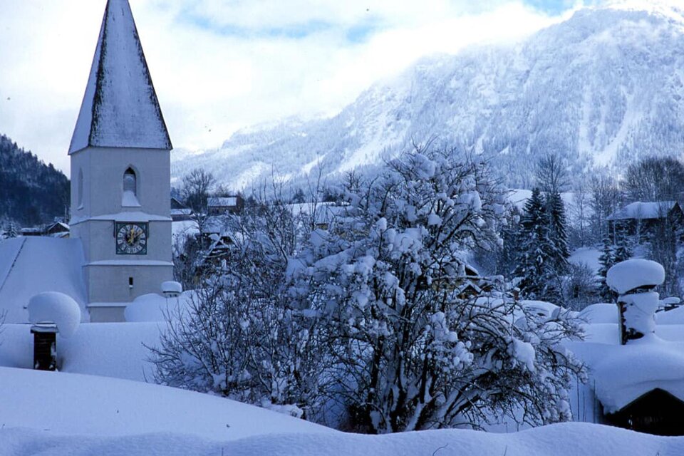Eine verschneite Landschaft mit einem hohen Kirchturm. Im Hintergrund sind Berge und ein winterlicher Himmel zu sehen. | © TVB Ausseerland Salzkammergut_Pirker