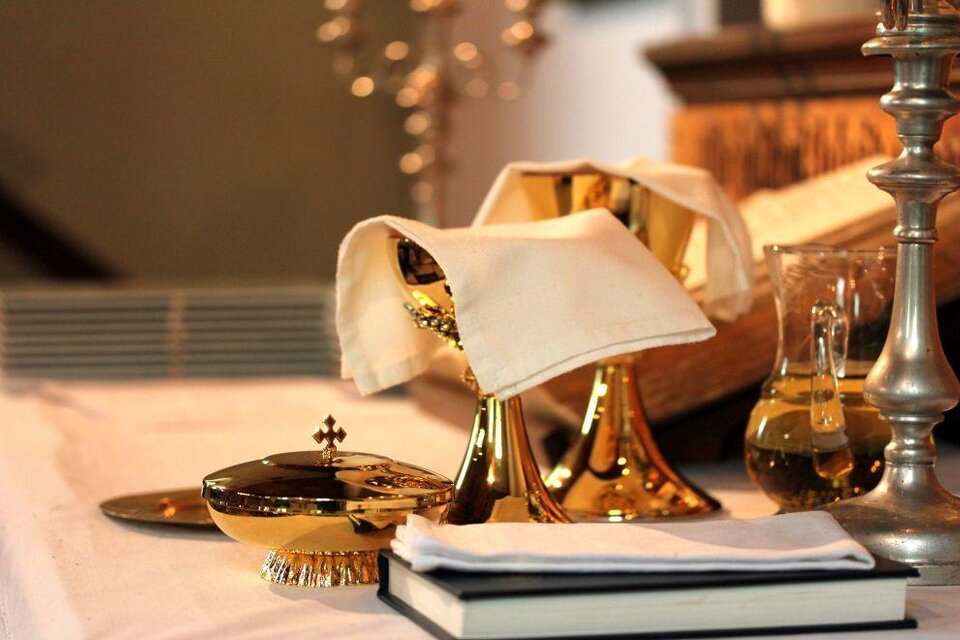Ein schön dekorierter Tisch mit goldenen religiösen Gefäßen und einem Buch. Neben den Gefäßen stehen ein Glas und ein Serviettenring. | © Tieber Doris