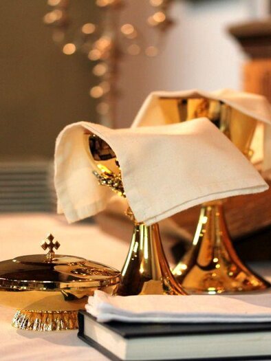 Ein schön dekorierter Tisch mit goldenen religiösen Gefäßen und einem Buch. Neben den Gefäßen stehen ein Glas und ein Serviettenring. | © Tieber Doris