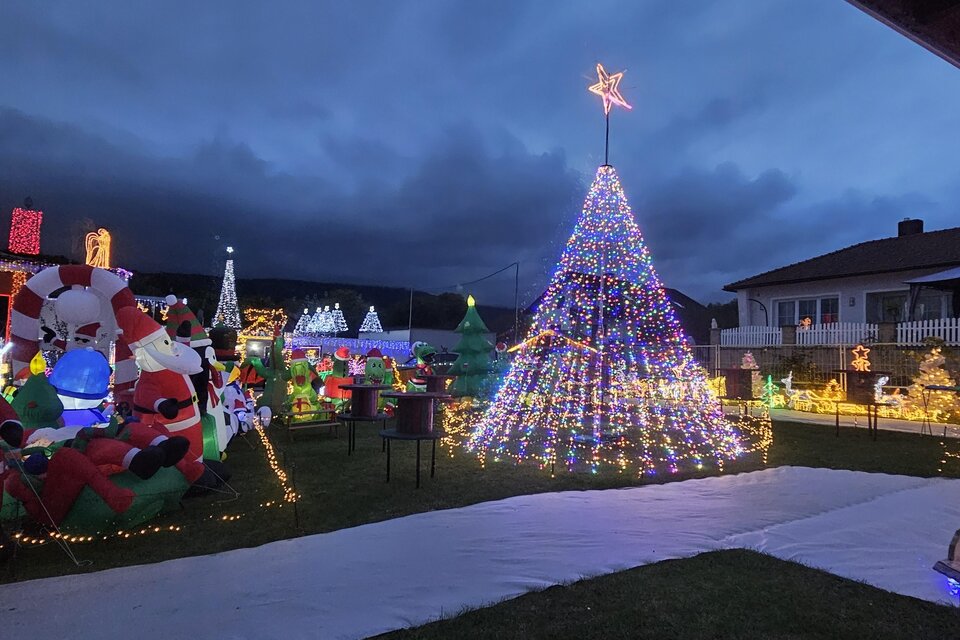 Ein festlich geschmückter Garten mit vielen Weihnachtslichtern und Figuren, darunter ein großer Weihnachtsbaum und verschiedene Weihnachtsmann-Dekorationen. Die Stimmung ist weihnachtlich und einladend. | © Wiesenhofer Stefan