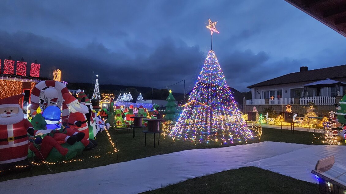 Ein festlich geschmückter Garten mit vielen Weihnachtslichtern und Figuren, darunter ein großer Weihnachtsbaum und verschiedene Weihnachtsmann-Dekorationen. Die Stimmung ist weihnachtlich und einladend. | © Wiesenhofer Stefan