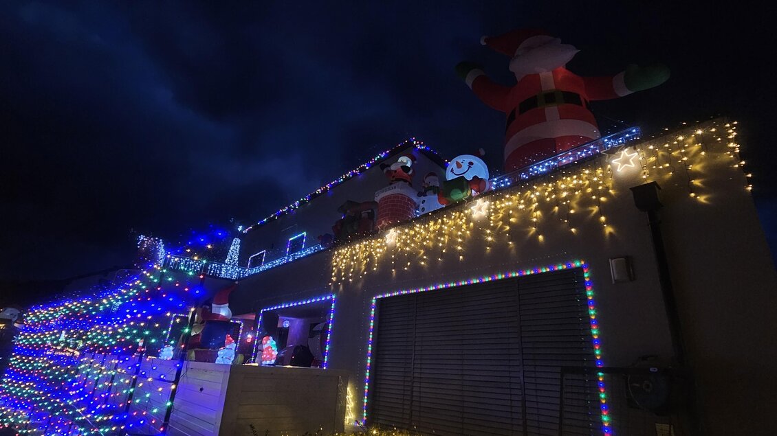 Ein festlich beleuchtetes Haus mit bunten Lichtern und Weihnachtsdekoration. Auf dem Dach stehen große Figuren von Santa Claus und anderen Weihnachtsmotiven. | © Wiesenhofer Stefan