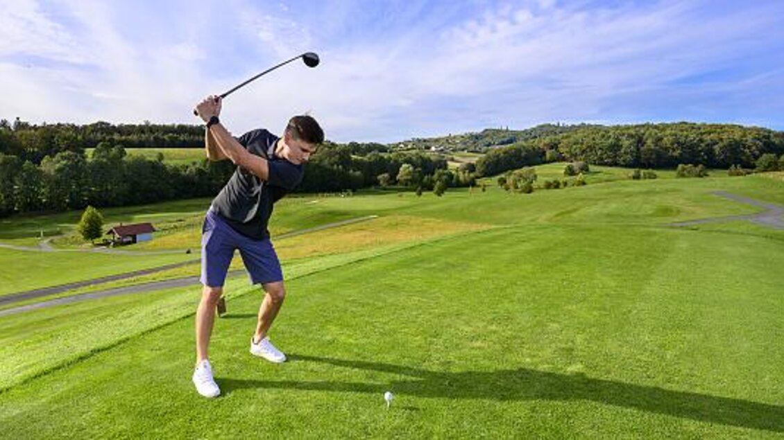 Ein Mann spielt Golf auf einem grünen Golfplatz. Im Hintergrund sind sanfte Hügel und ein blauer Himmel sichtbar. | © TV Thermen- & Vulkanland