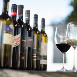 Eine Auswahl an Weinflaschen steht auf einem Tisch. Neben den Flaschen stehen zwei Weingläser, eines mit Rotwein und das andere mit Weißwein. | © Garten Hotel Ochensberger