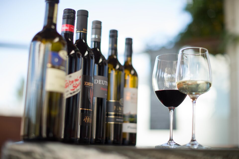 Eine Auswahl an Weinflaschen steht auf einem Tisch. Neben den Flaschen stehen zwei Weingläser, eines mit Rotwein und eines mit Weißwein.
