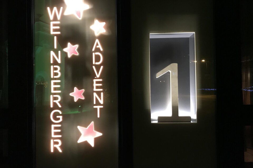 Beleuchtetes Adventfenster mit Sternen, dem Schriftzug „Weinberger Advent“ und der leuchtenden Zahl 1 in stimmungsvoller Abendatmosphäre.
 | © Rudolf Kainz