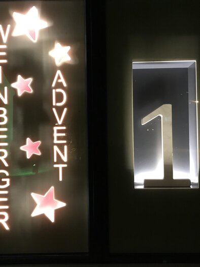 Illuminated Advent window with stars, the inscription "Weinberger Advent" and the glowing number 1 in a cozy evening atmosphere. | © Rudolf Kainz