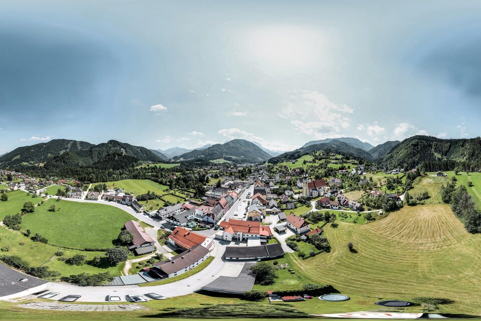Eine malerische Ansicht eines kleinen Dorfes umgeben von Bergen und grünen Wiesen. Der Himmel ist teilweise bewölkt und der Ort strahlt eine ruhige Atmosphäre aus. | © TV Gesäuse