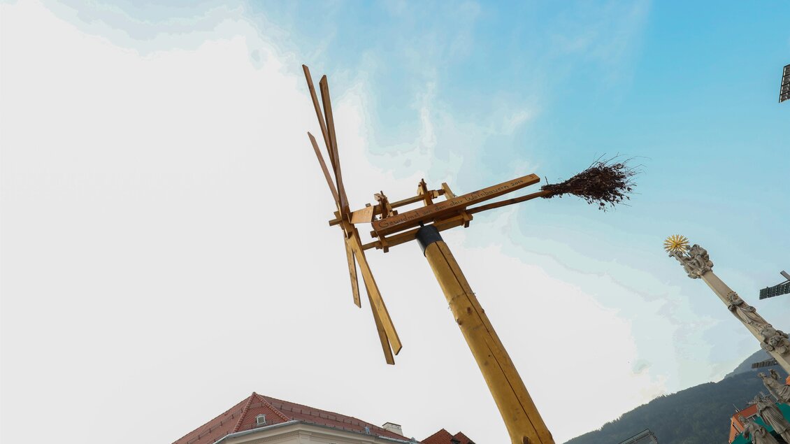 Ein Holzgerüst mit einem drehbaren Windrad und einer Besenbinde darauf. Der Himmel ist klar und blau. | © Foto Freisinger
