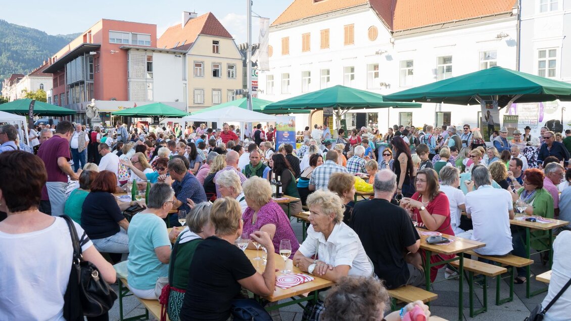 Ein belebter Marktplatz mit vielen Menschen, die an Tischen sitzen. Es gibt grüne Sonnenschirme und Feststimmung in der Luft. | © Foto Freisinger