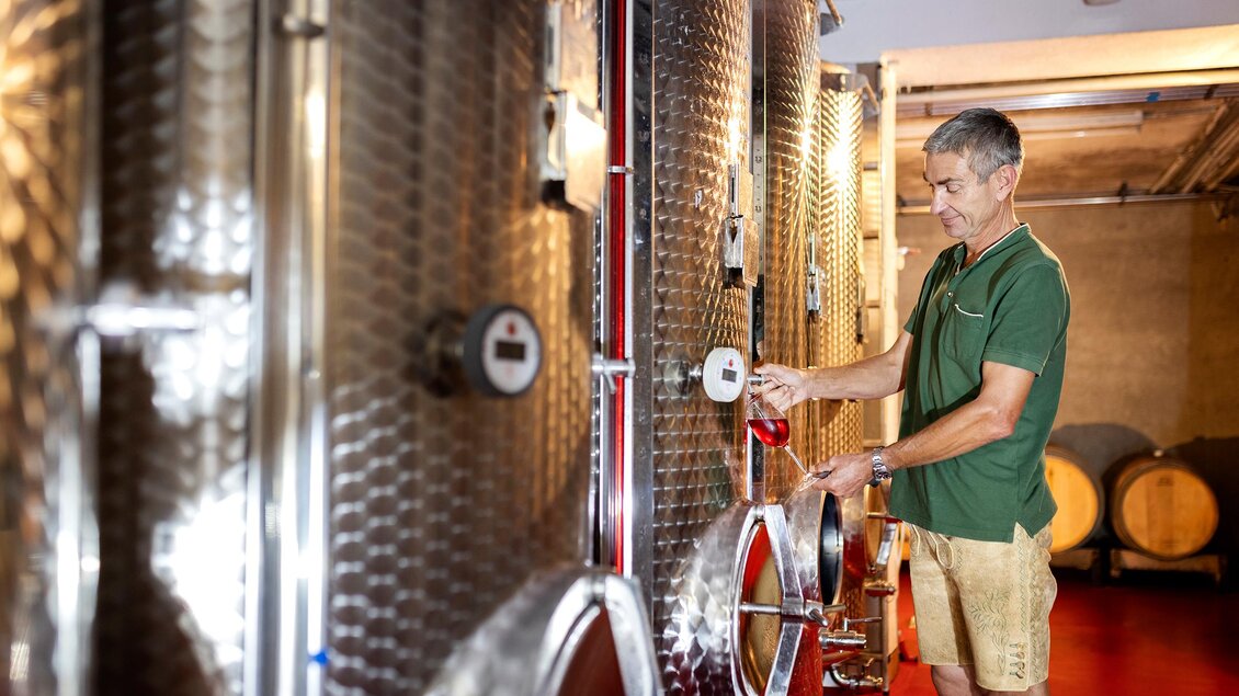 Ein Mann füllt Wein aus einem großen Edelstahltank in ein Glas. Im Hintergrund sind weitere Weintanks und Holzfässer zu sehen. | © @Netzwerk Kulinarik Harald Eisenberger