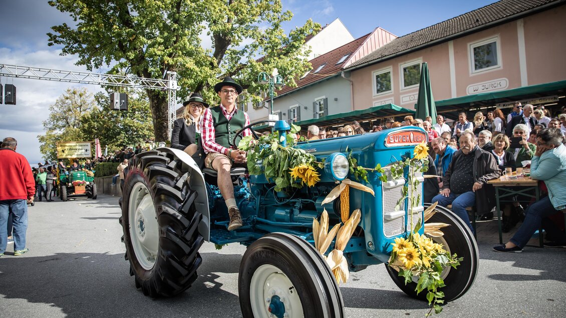 Ein festlich geschmückter Traktor fährt durch eine belebte Straße. Im Hintergrund stehen Zuschauer und feiern das Ereignis. | © Achromatic Photography