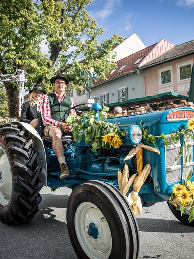 A festively decorated tractor drives through a busy street. In the background, spectators stand and celebrate the event. | © Achromatic Photography