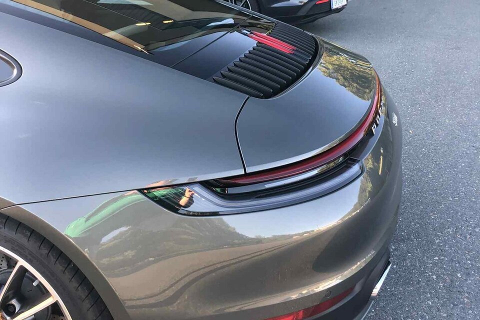 Drei Sportwagen, darunter ein grauer Porsche und ein gelber Coupé, stehen auf einem Parkplatz.