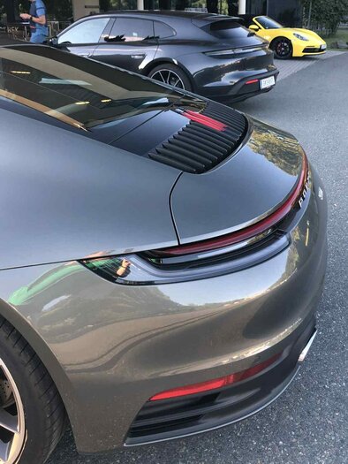 Drei Sportwagen, darunter ein grauer Porsche und ein gelber Coupé, stehen auf einem Parkplatz.