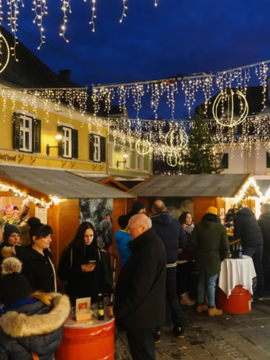 Ein festlicher Weihnachtsmarkt mit zahlreichen Menschen und festlicher Beleuchtung. Die Stände bieten Getränke und Leckereien in einer gemütlichen Atmosphäre.