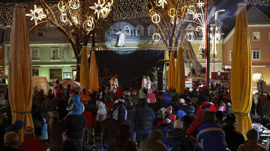 Ein festlicher Weihnachtsmarkt mit einer großen Menschenmenge. Die Szenerie ist von Lichtern und Sternen geschmückt, während auf einer Bühne eine Aufführung stattfindet. | © Tourismusverband Oststeiermark