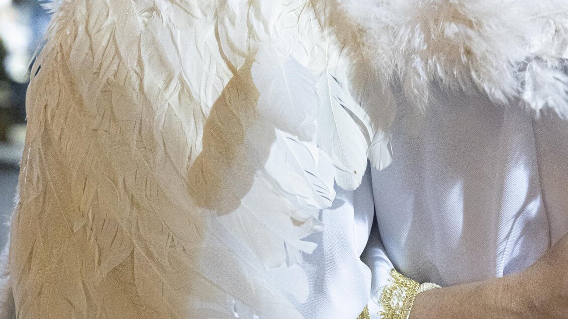 Ein elegantes Kostüm mit weißen Engelsflügeln. Die Person trägt ein schlichtes, weißes Gewand mit goldenen Akzenten.