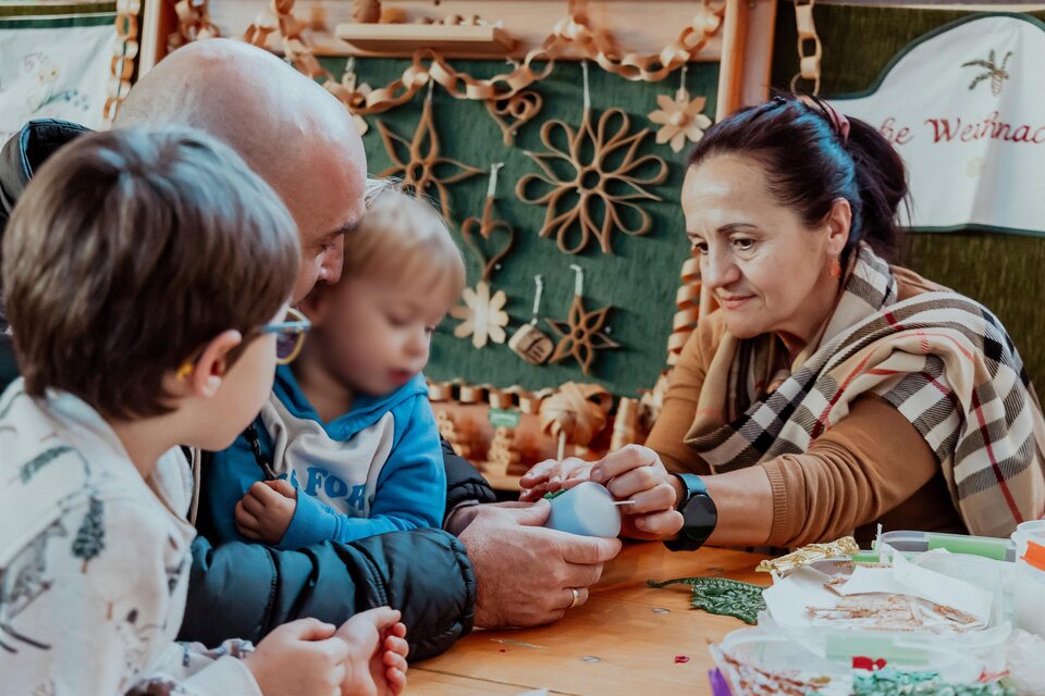 Eine Familie bastelt zusammen an einem Tisch. Zwei Kinder und ein Erwachsener arbeiten gemeinsam an einem Projekt.