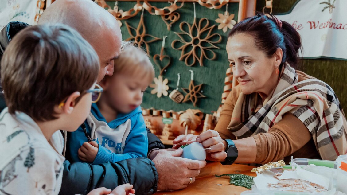 Eine Familie bastelt zusammen an einem Tisch. Zwei Kinder und ein Erwachsener arbeiten gemeinsam an einem Projekt.